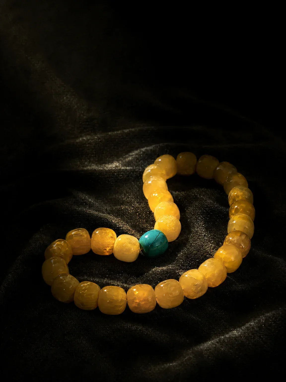 OresGreen Glow Bracelet: A premium translucent honey amber resin bead bracelet featuring a single natural blue turquoise center stone, elegantly styled on a black velvet background under dramatic low-key lighting.