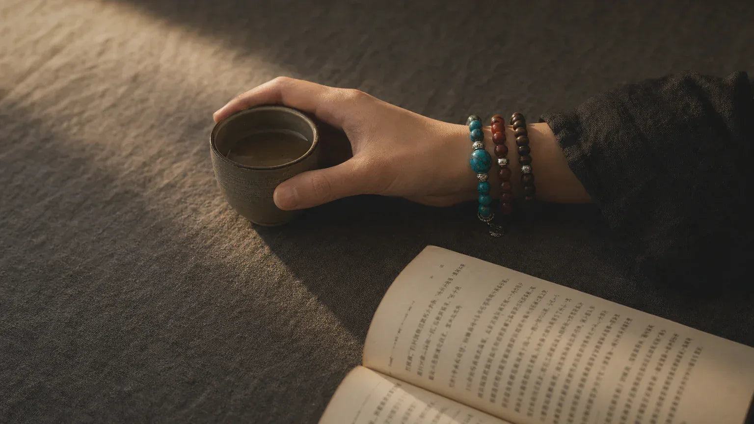 Premium handcrafted gemstone bracelet stack for men and women by OresGreen, styled with a pottery tea cup, dark linen clothing, and a book for quiet zen meditation and daily mindfulness rituals.