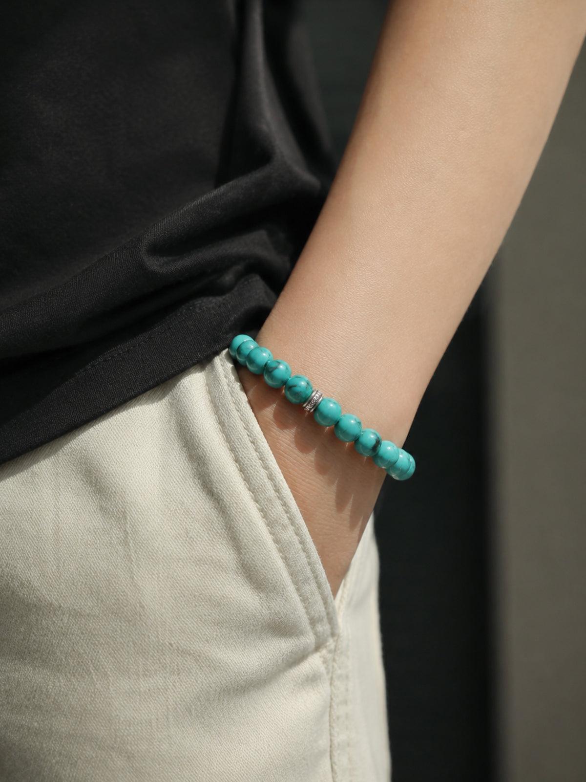 OresGreen Stillness Bracelet: A minimalist natural blue turquoise beaded stone bracelet with silver accents worn on a wrist, styled with casual white linen pants for a modern zen look.