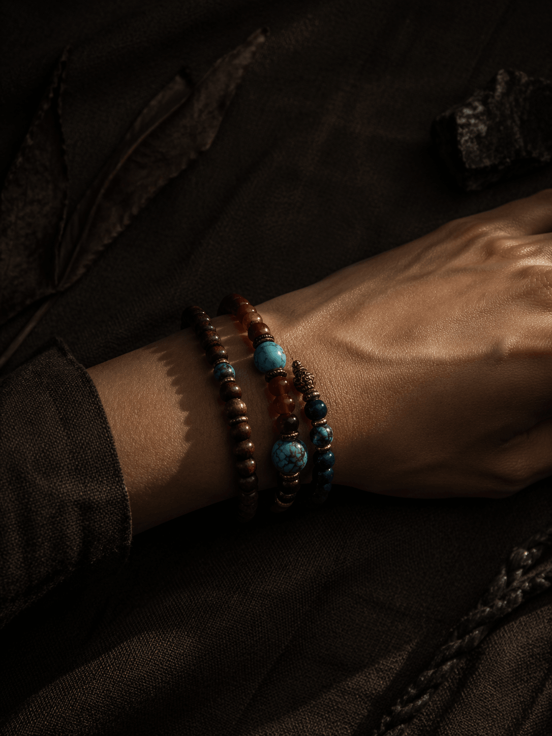 OresGreen layered jewelry style: A person wearing a stack of Grounded green sandalwood and natural blue turquoise beaded stone bracelets on their wrist, beautifully captured under dramatic moody shadows and vintage dark clothing.