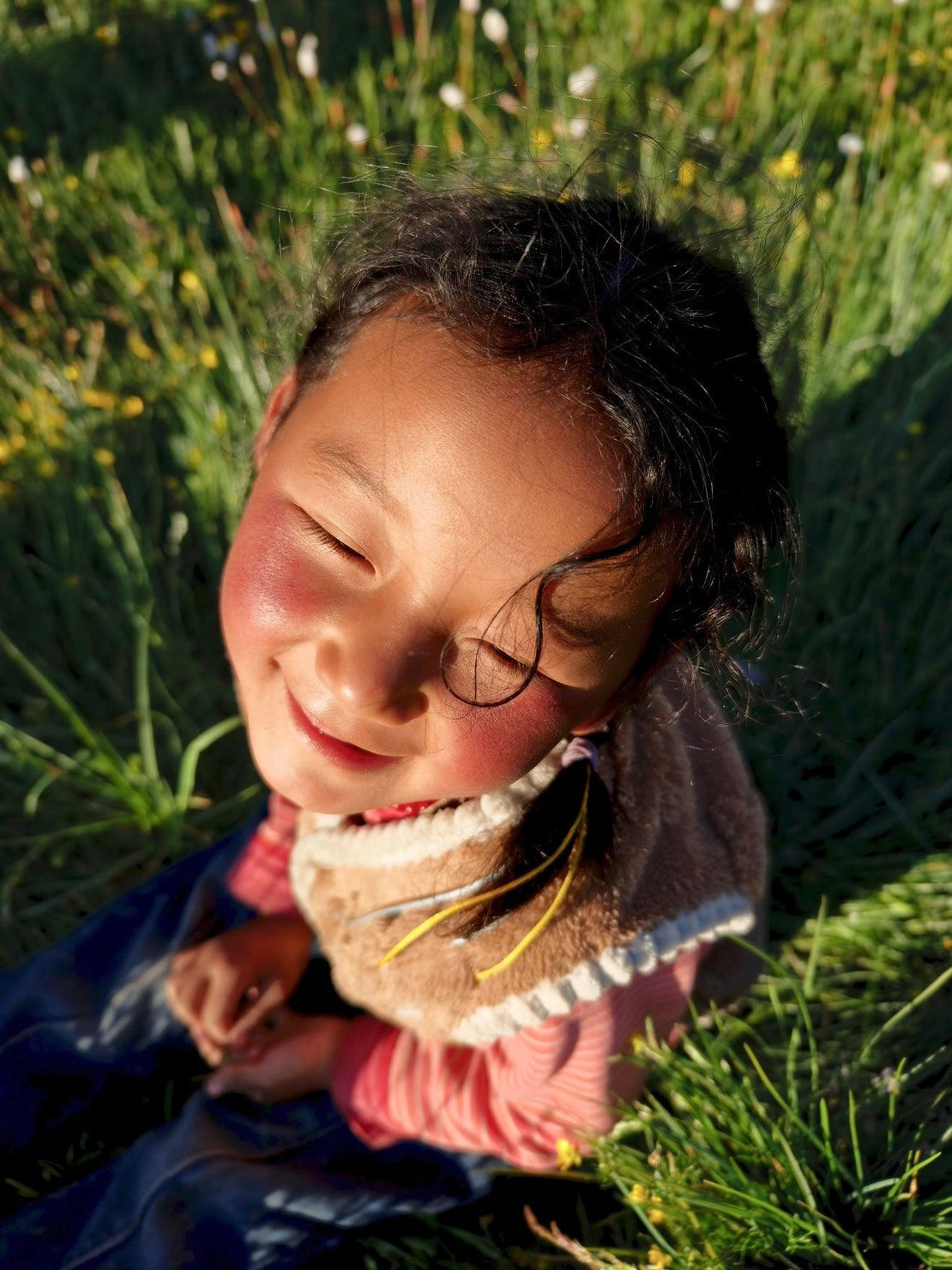 OresGreen social impact: Close-up of a smiling local Tibetan child basking in the warm golden sunlight on a lush green Himalayan meadow, representing the brand's heartful charity mission.